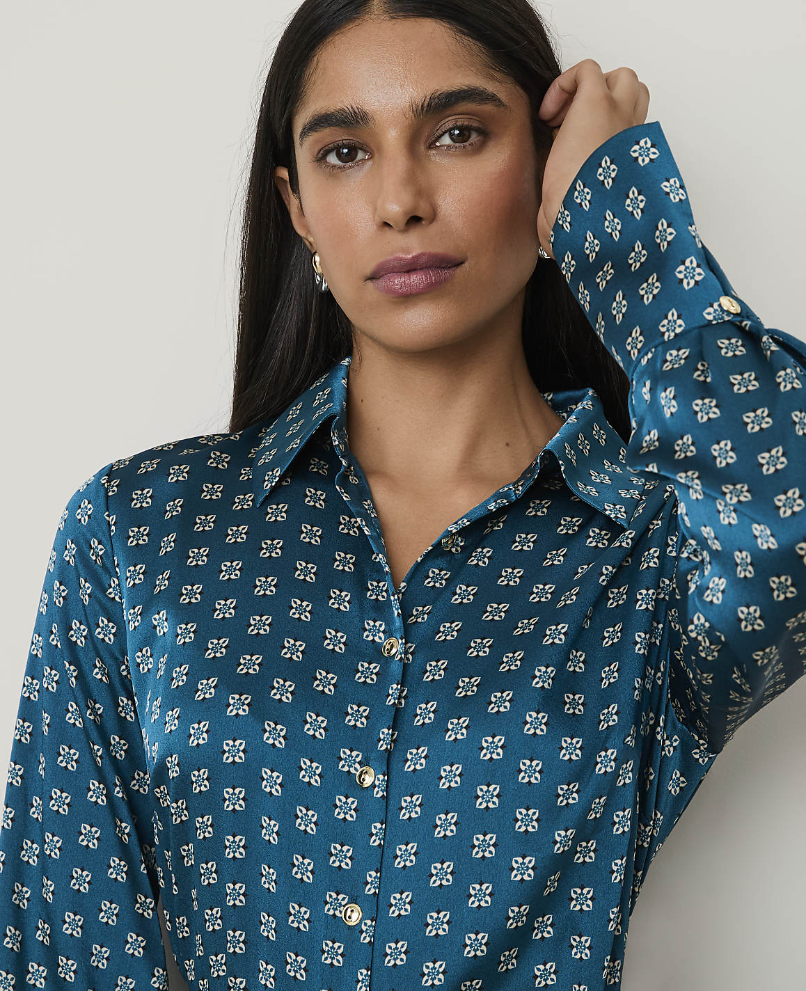 A woman with dark hair and a patterned teal shirt is shown against a plain white background.