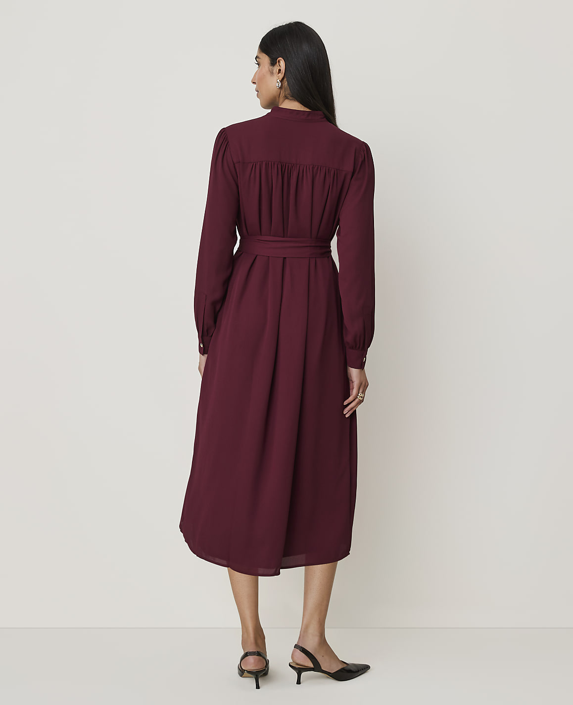 A woman in a burgundy dress stands against a plain, light-colored background.