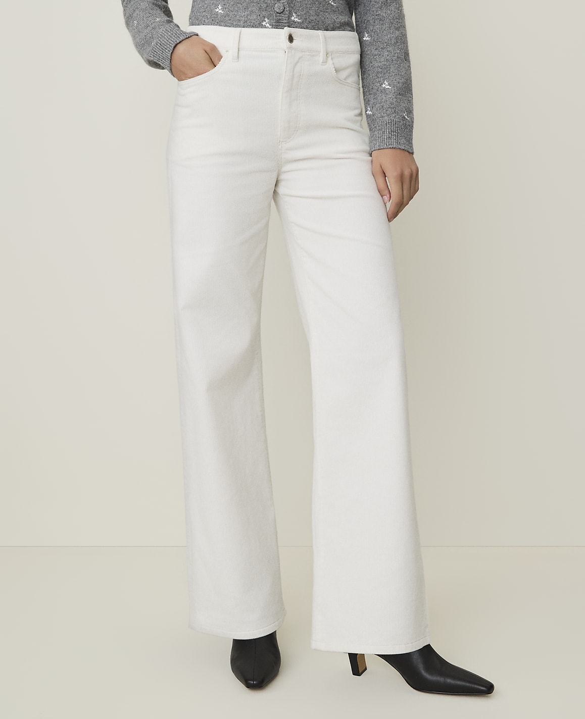 A person wearing white wide-leg pants and black heeled boots stands against a plain, light-colored background.