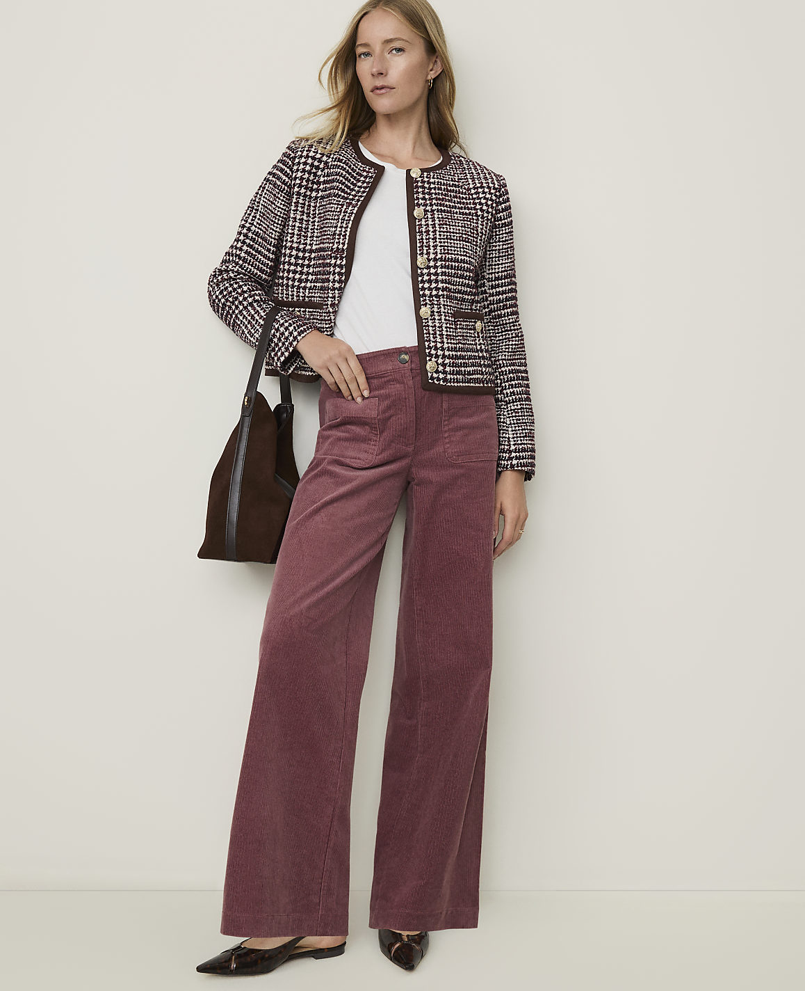 A woman in a tweed jacket and wide-leg corduroy pants stands against a plain, light-colored background.