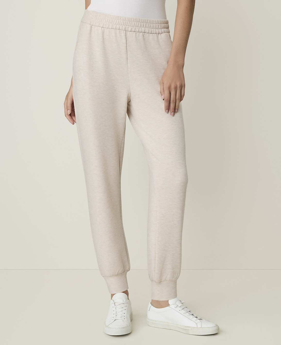 A person stands in light-colored sweatpants and white sneakers against a plain, light background.