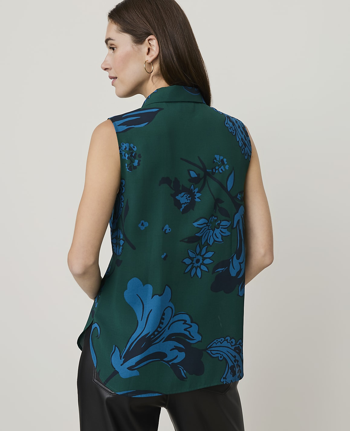 A woman in a green floral sleeveless shirt stands against a plain white background.