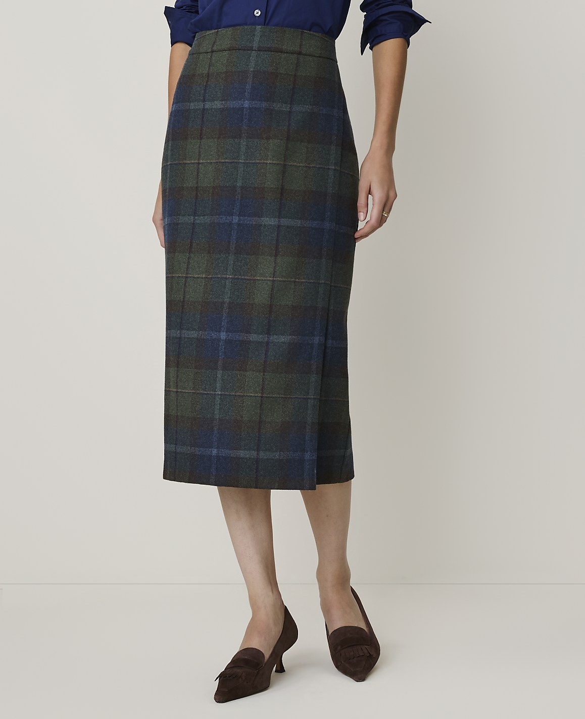 A woman models a green and blue plaid pencil skirt with brown loafers against a plain, light background.