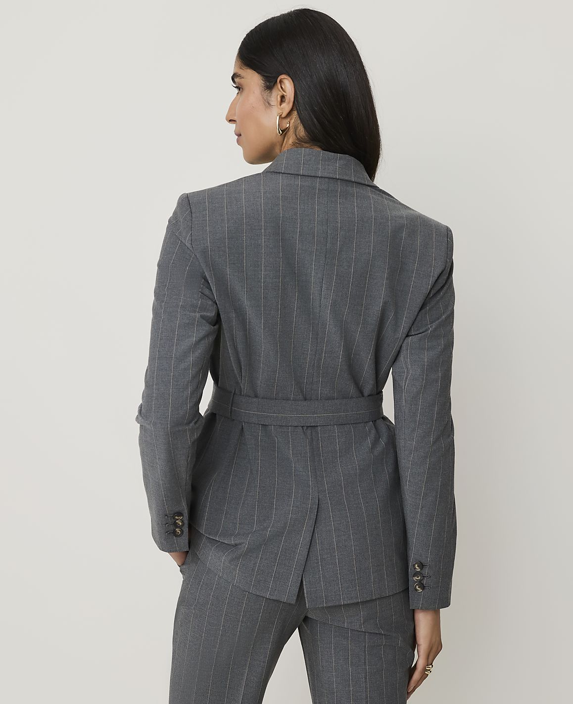 A woman in a pinstripe suit stands against a plain, light gray background.