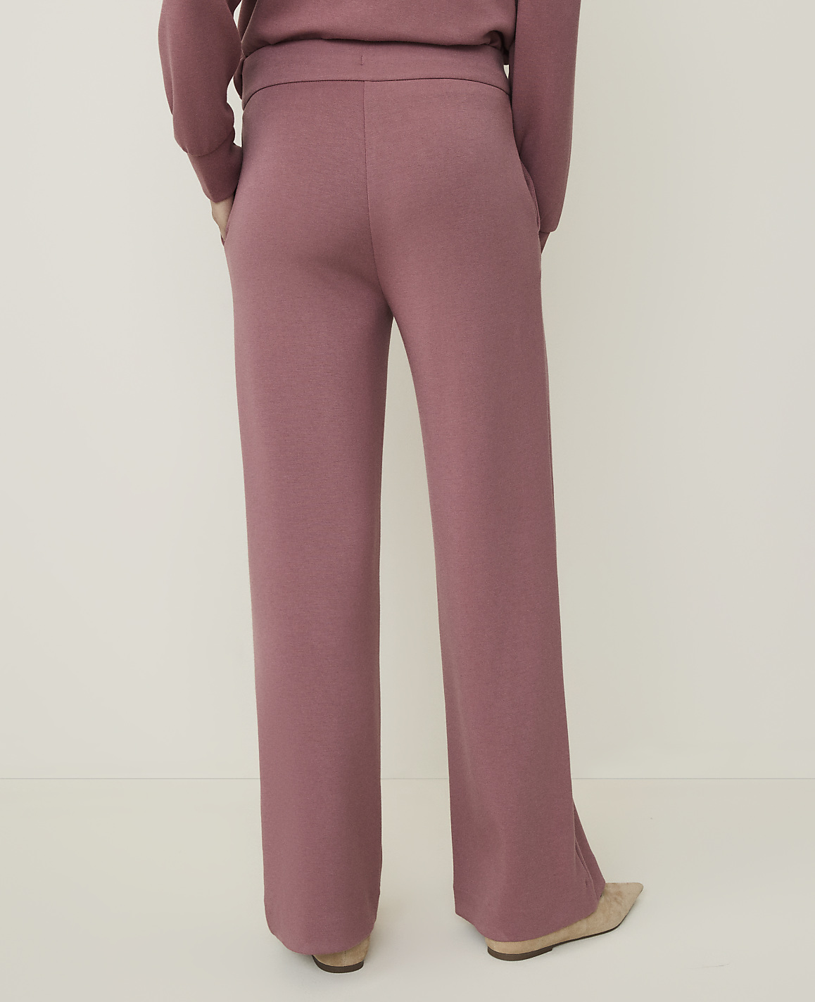 A person wearing rose-colored knit pants stands against a plain, light-colored background.
