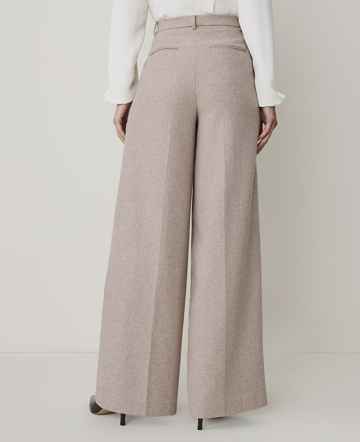 A person wearing wide-leg beige trousers and a white blouse stands against a plain, light-colored background.