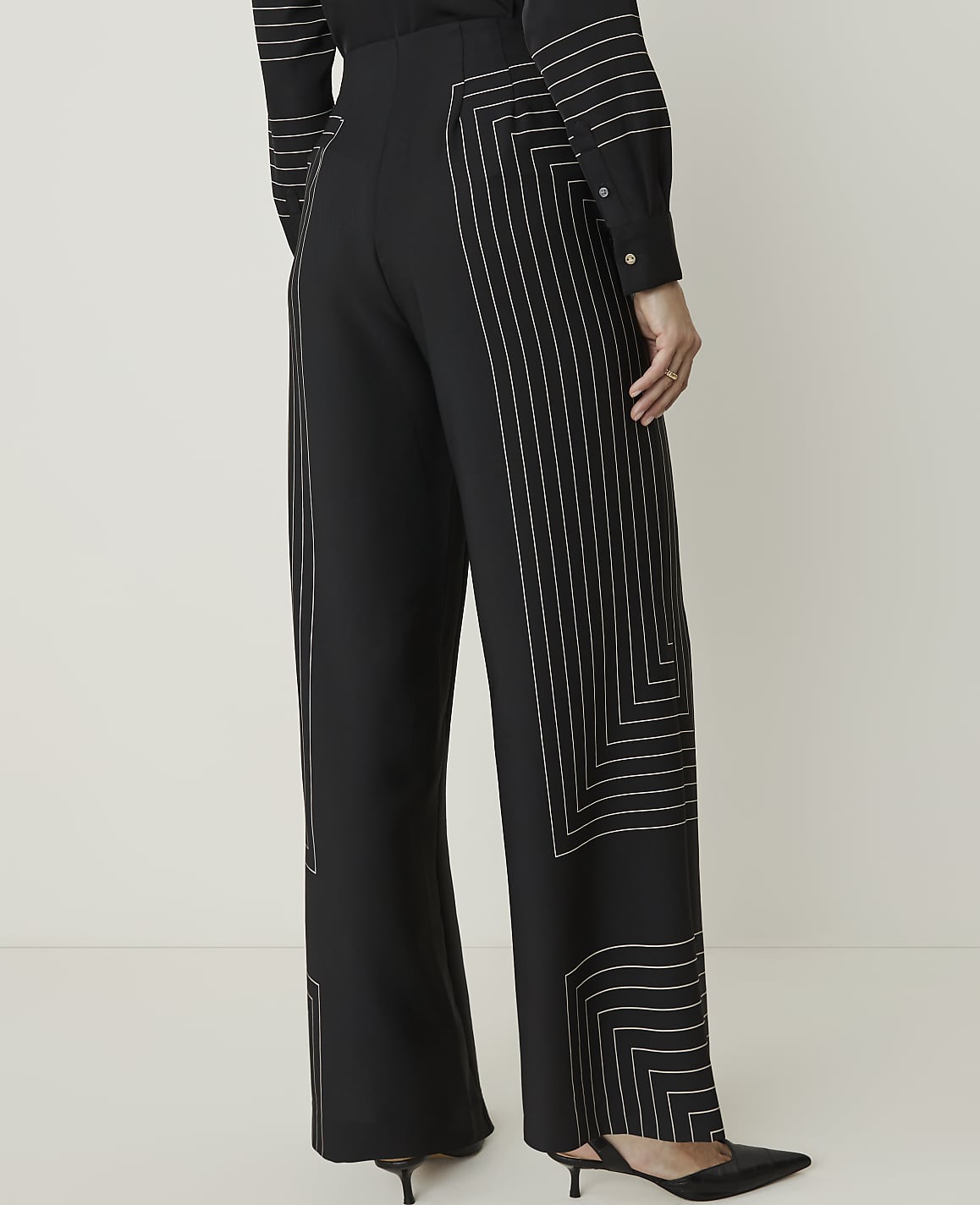 A person wearing black wide-leg pants with geometric white stitching stands against a plain white background.