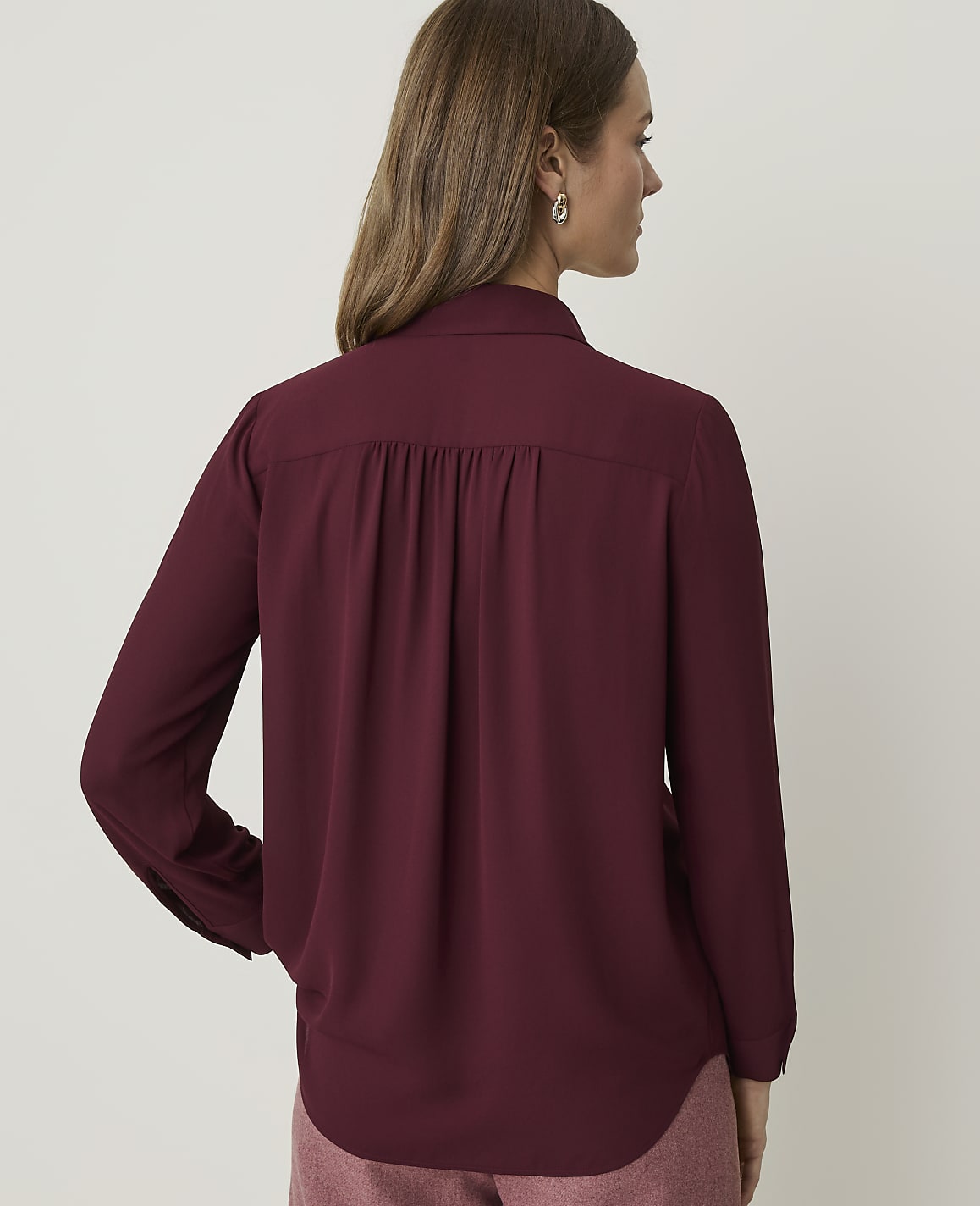 A woman in a maroon blouse stands against a plain, light-colored background.