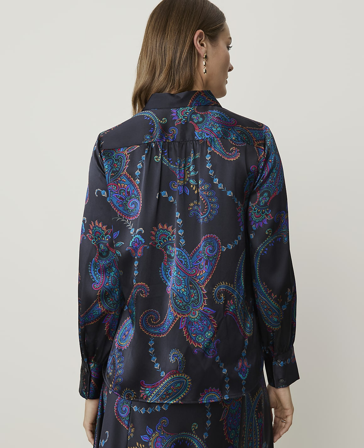 A woman in a dark, patterned blouse stands against a plain background.