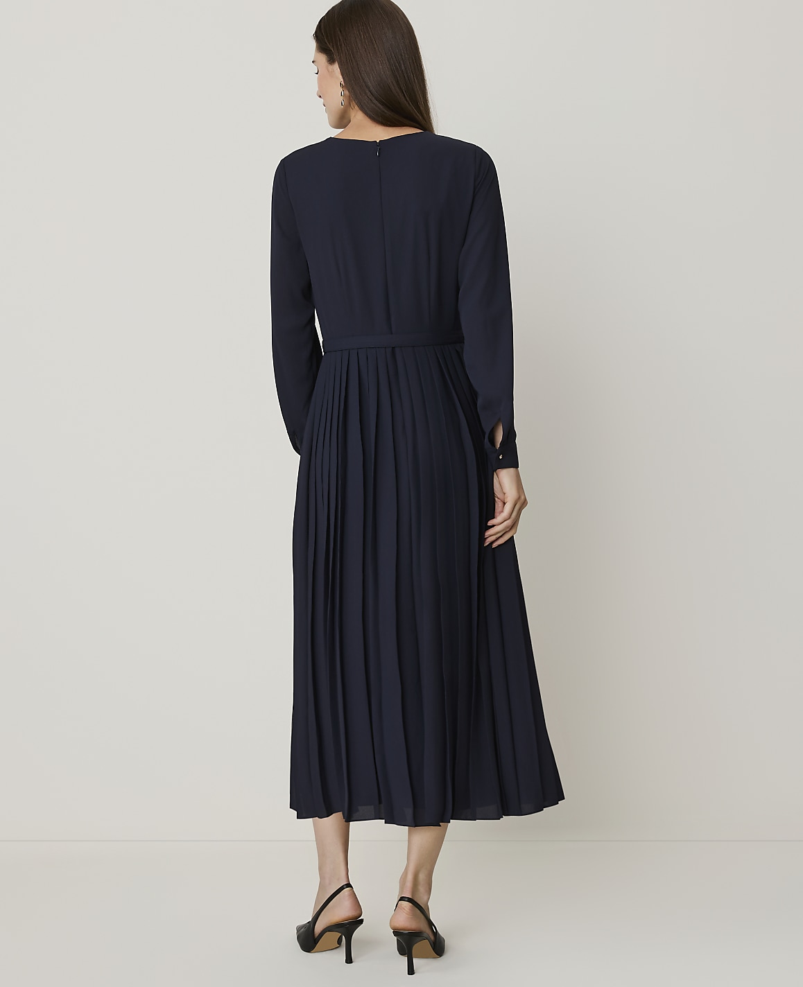 A woman in a navy pleated dress stands against a plain, light-colored background.