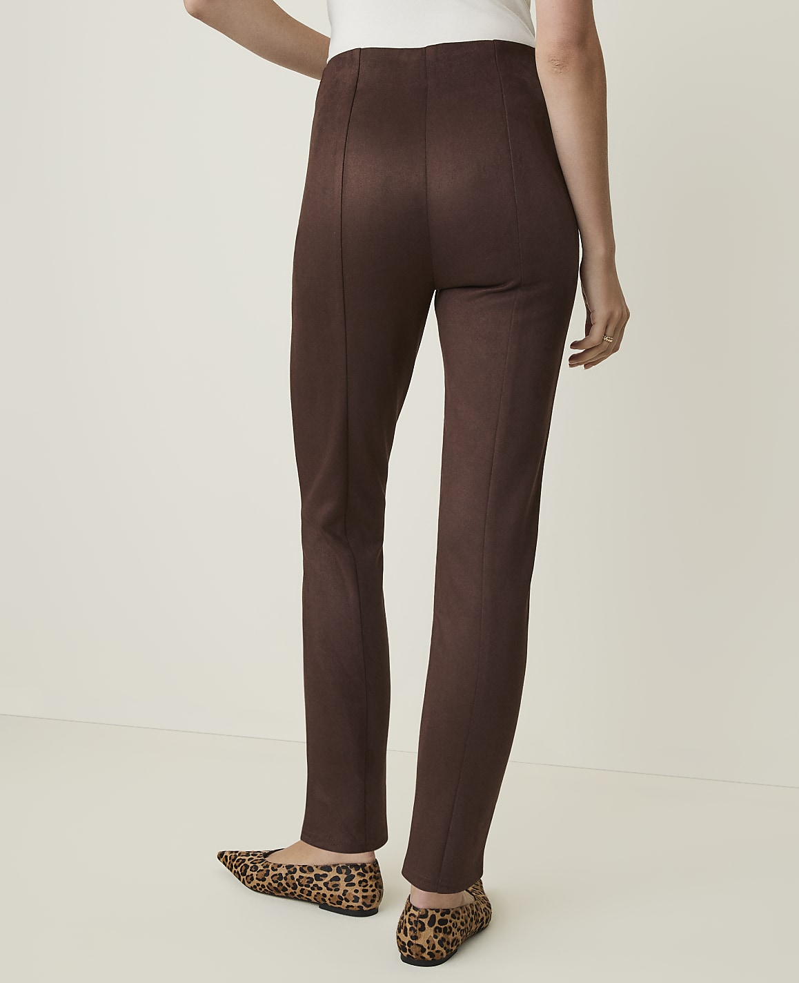 A person wearing brown leggings and leopard print flats stands against a plain, light-colored background.