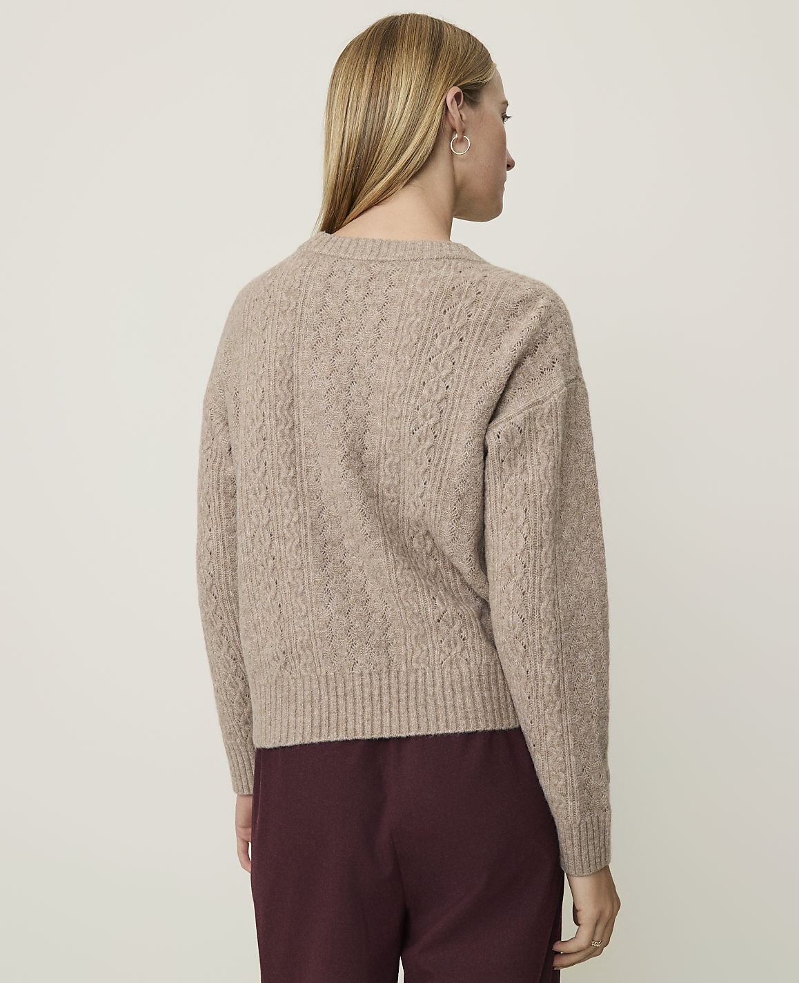 A woman in a cable-knit sweater stands against a plain, light-colored background.