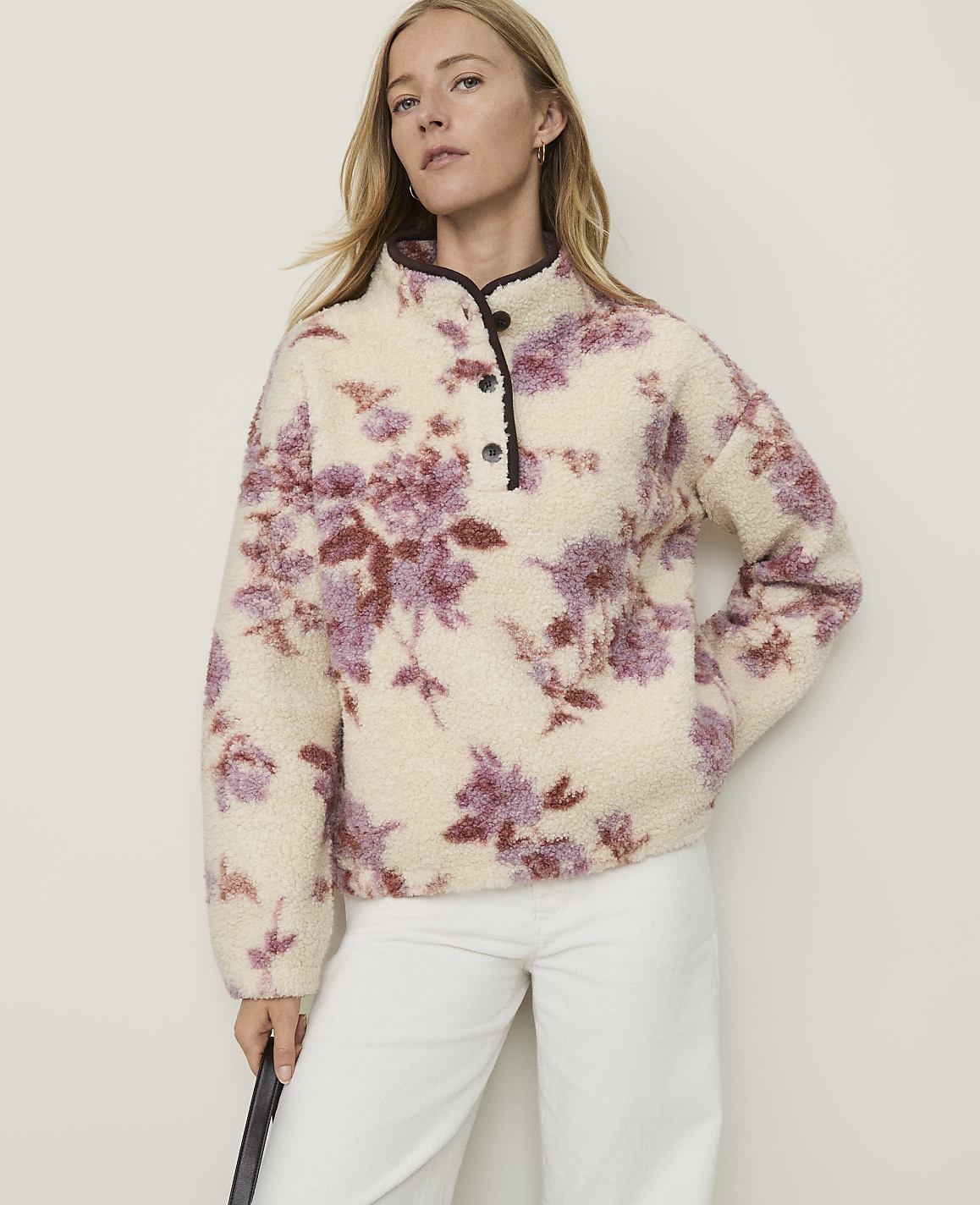 A woman in a cream-colored floral fleece pullover stands against a plain, light-colored background.