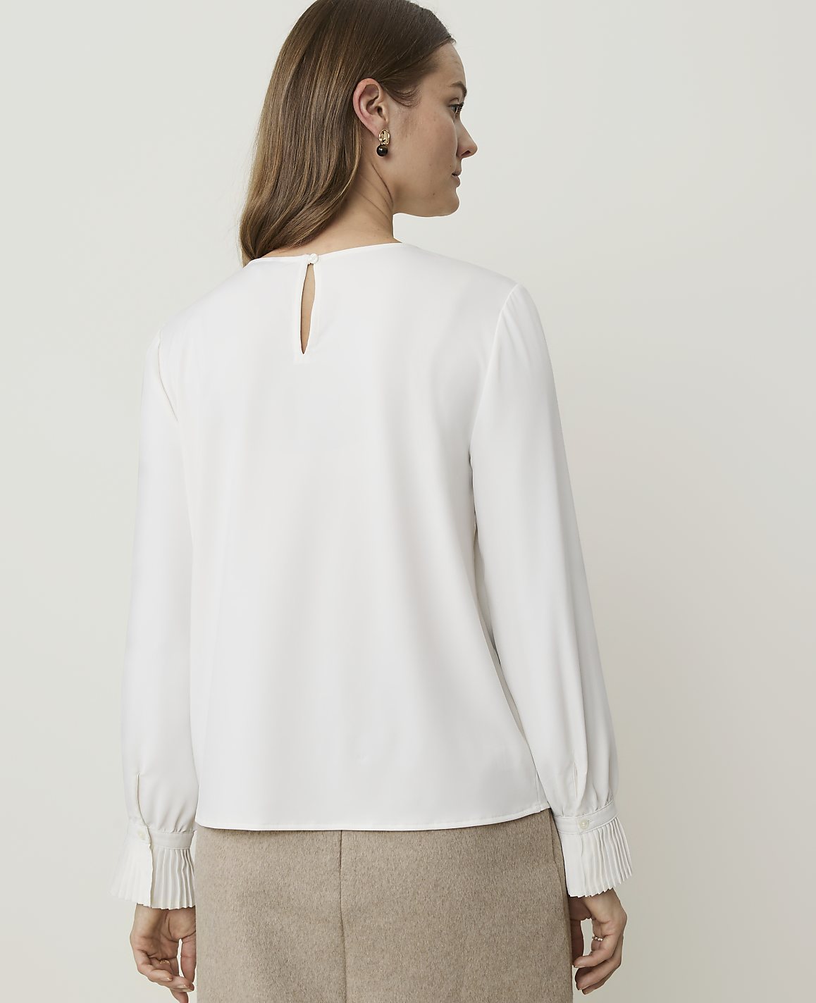 A woman in a white blouse and tan skirt stands against a plain, light-colored background.