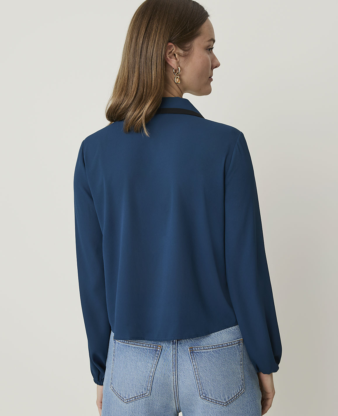 A woman in a teal blouse and jeans stands against a plain white background.