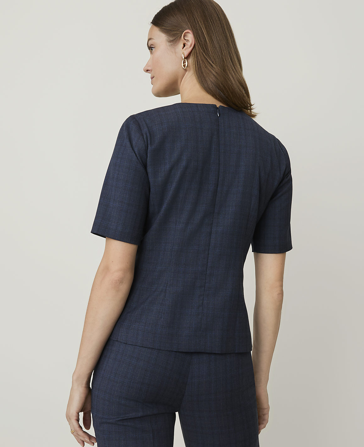 A woman in a navy plaid suit stands against a plain, light gray background.