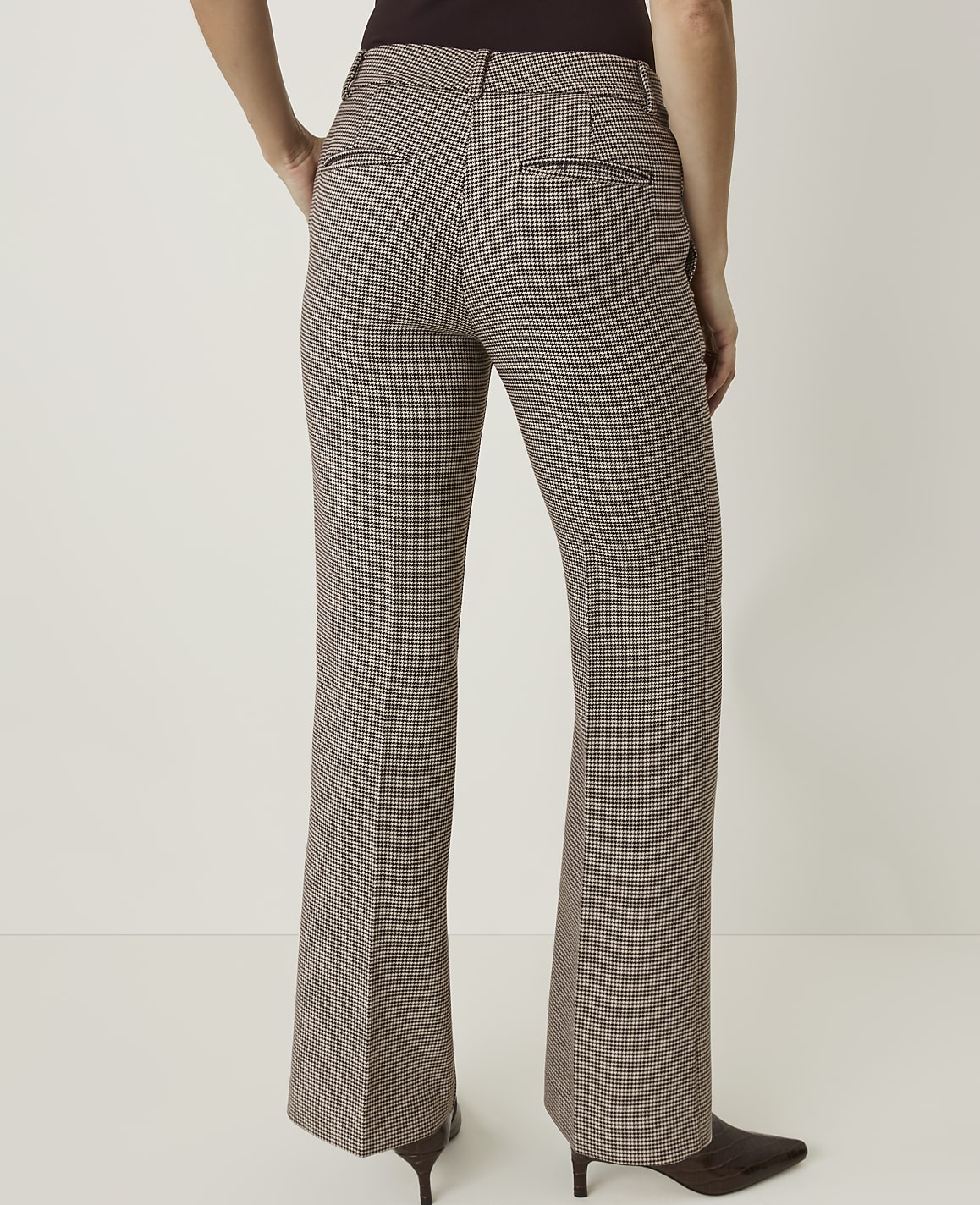 A person wearing brown and white checkered flared pants stands against a plain white background.