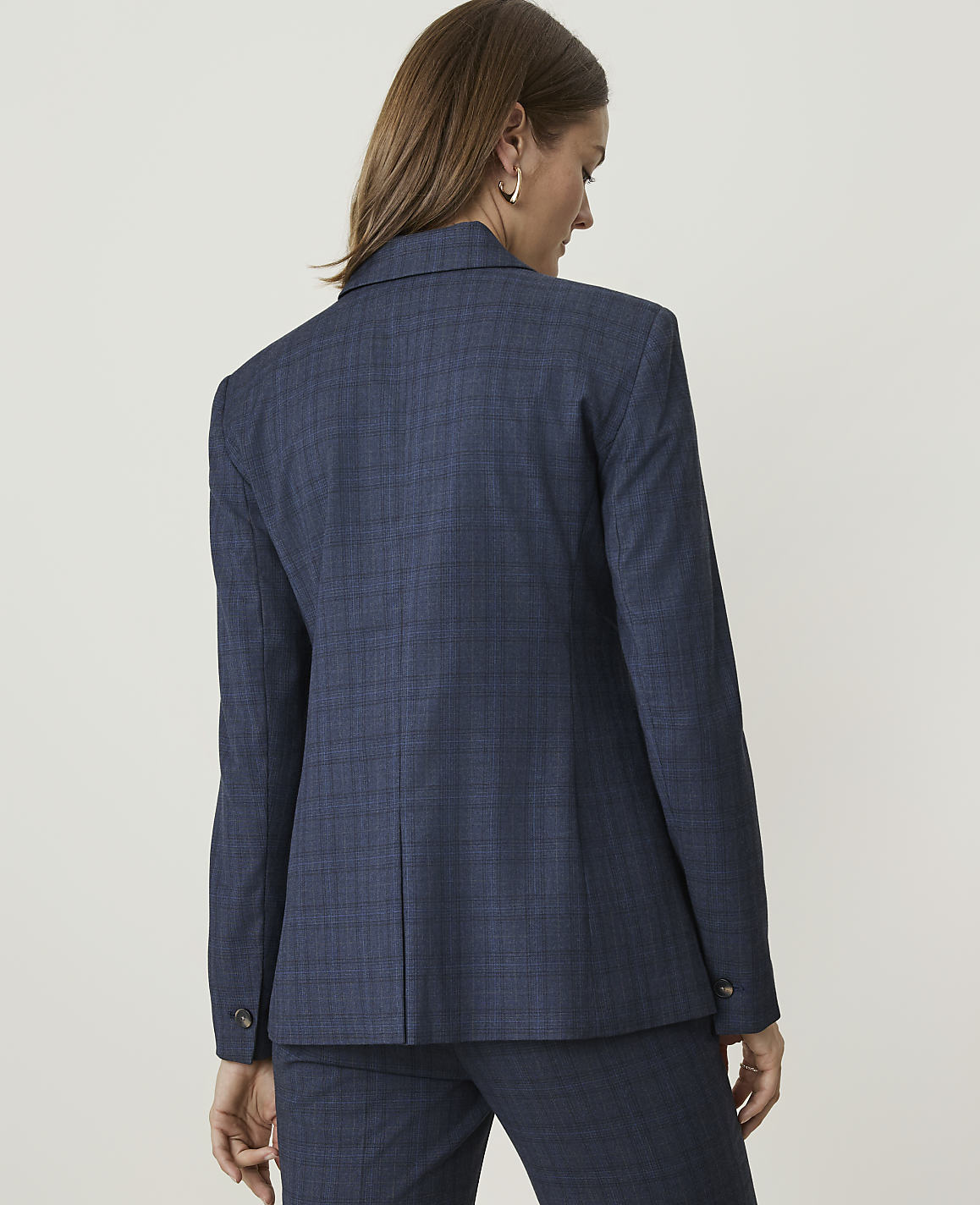 A woman in a blue plaid blazer and matching pants stands against a plain white background.