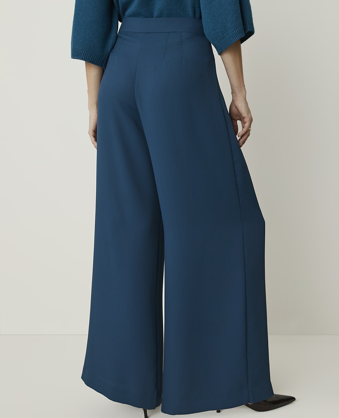 A person wearing teal wide-leg pants stands against a plain, light-colored background.