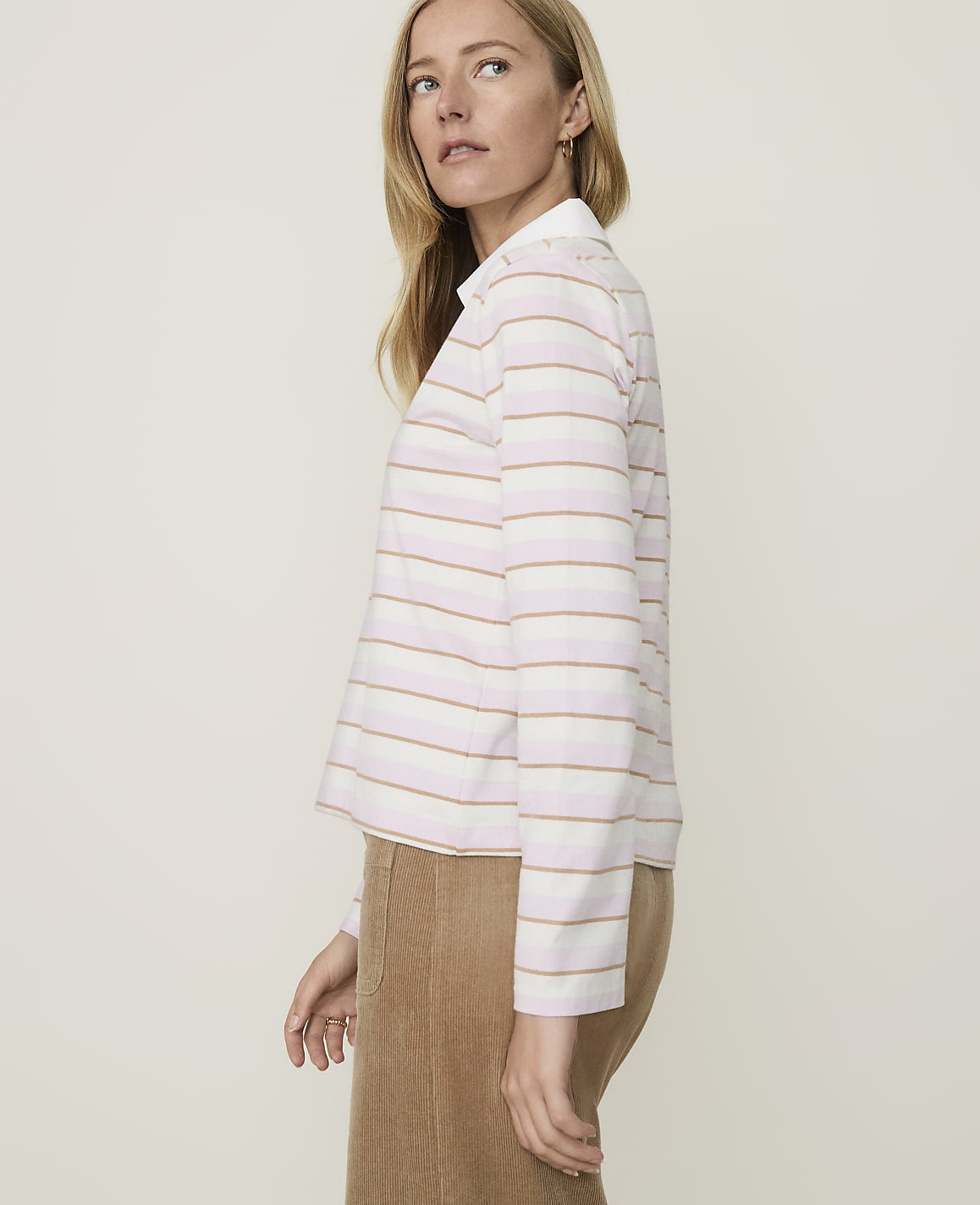 A woman in a striped shirt and corduroy skirt stands against a plain, light background.