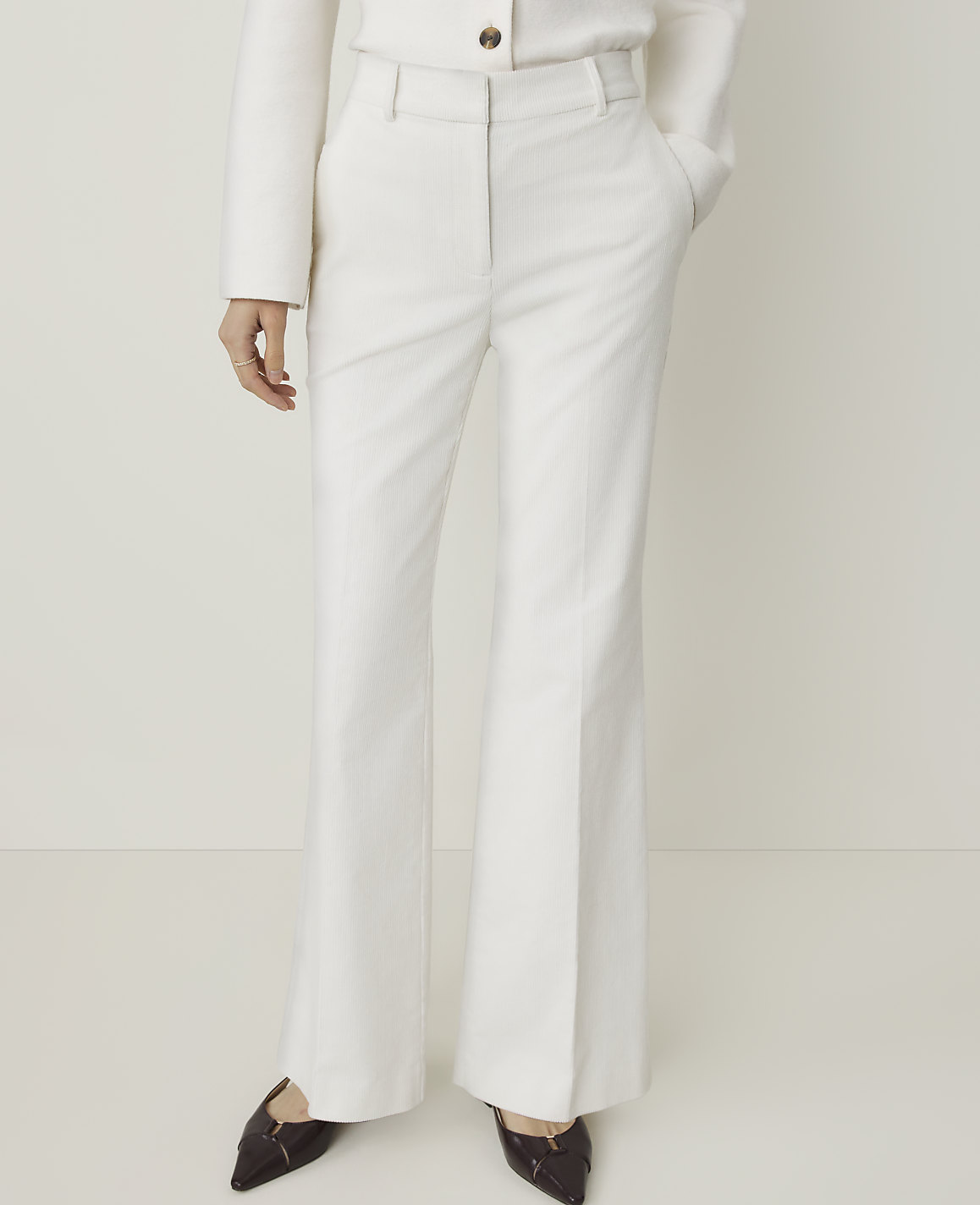 A person stands in white flared trousers and dark pointed shoes against a plain white background.