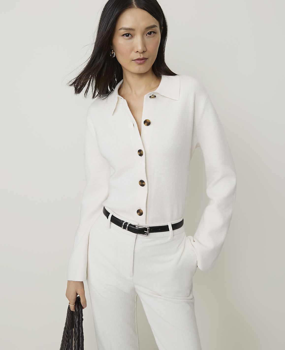 A woman in a white cardigan and pants stands against a plain white background.