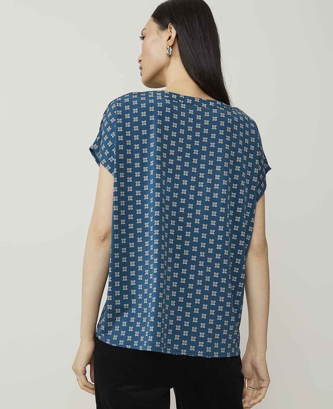 A woman in a patterned teal shirt stands against a plain white background.