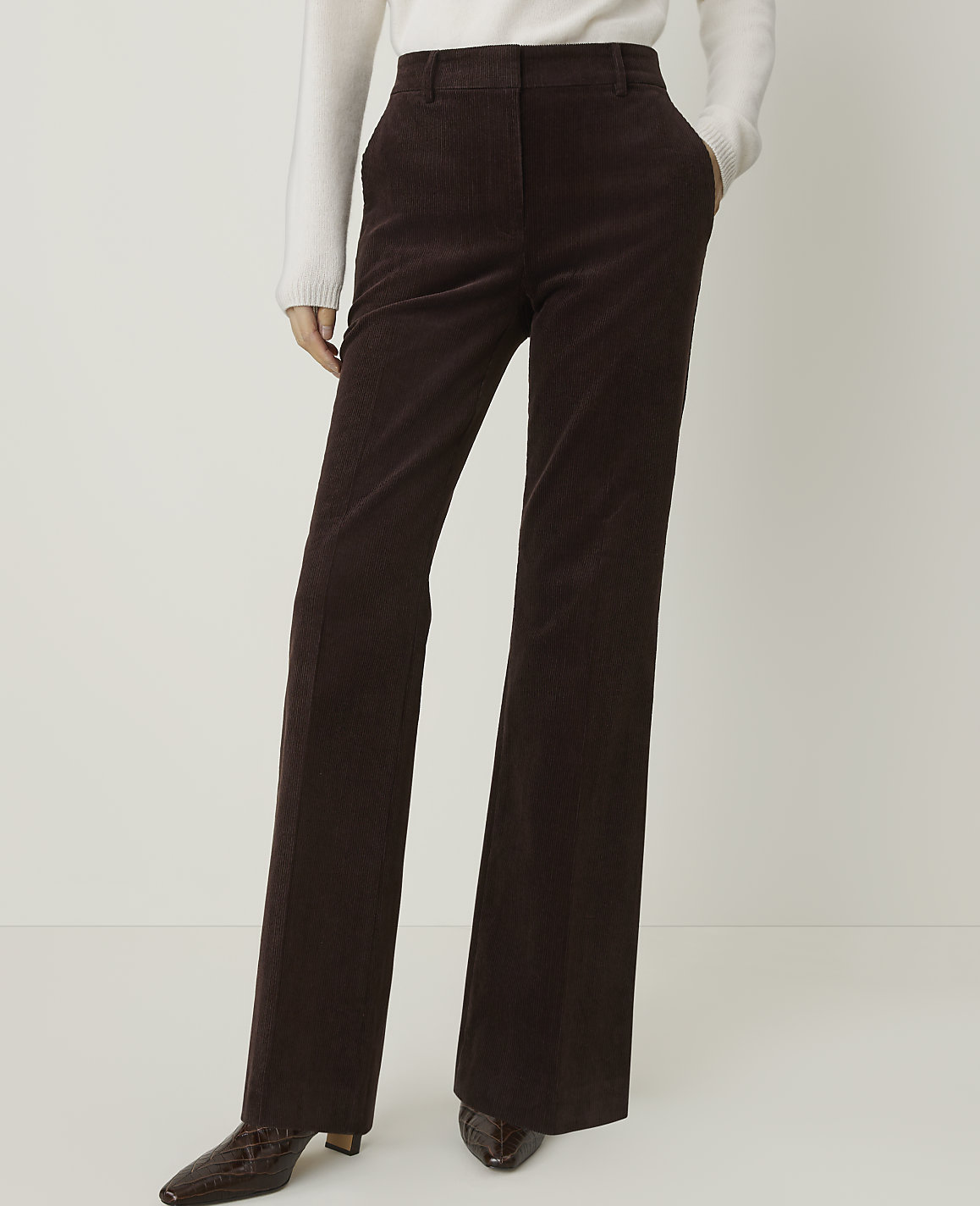 A person in brown corduroy pants and a white sweater stands against a plain white background.