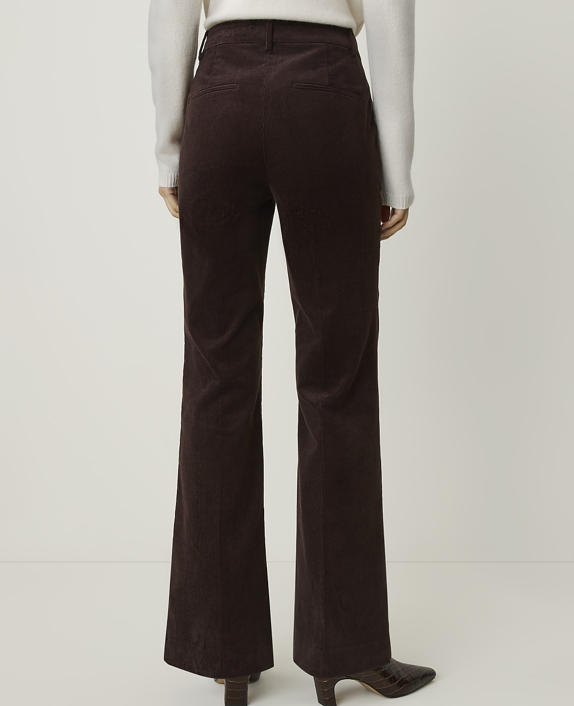 A person wearing brown corduroy pants and a white sweater stands against a plain white background.