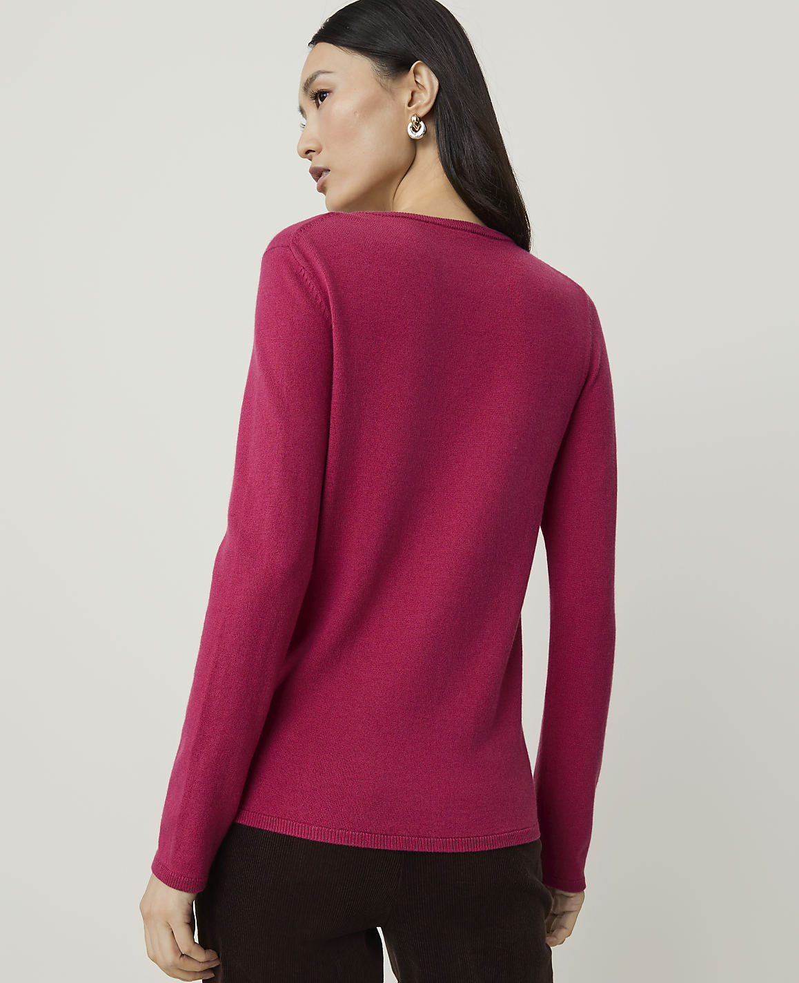 A woman in a pink sweater stands against a plain, light brown background.