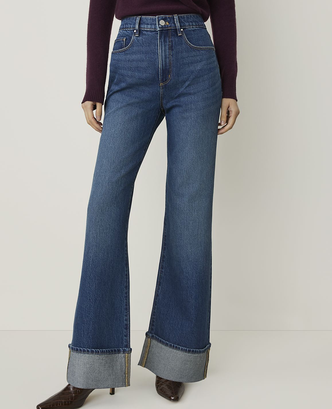 A person wearing high-waisted, flared jeans with large cuffs stands against a plain white background.