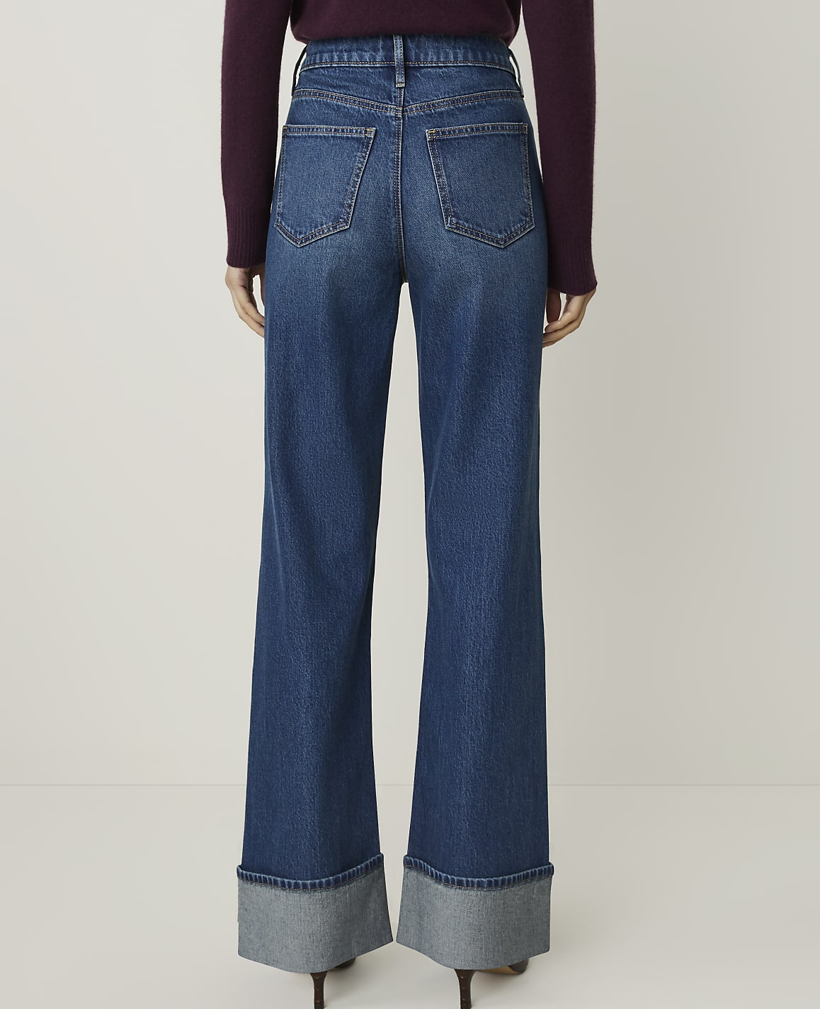 A person wearing wide-leg denim jeans with cuffed hems stands against a plain white background.