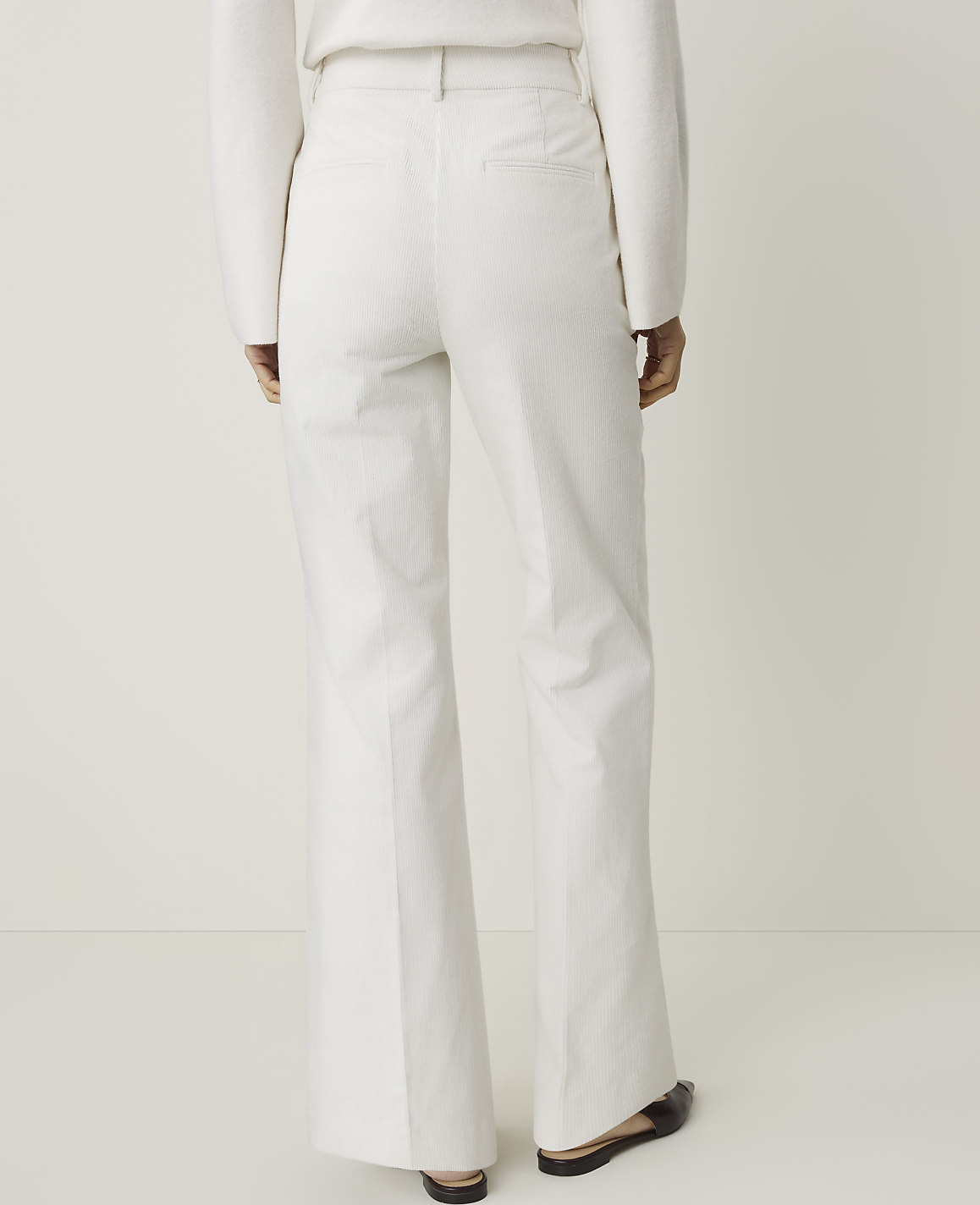A person wearing white flared trousers stands against a plain white background.