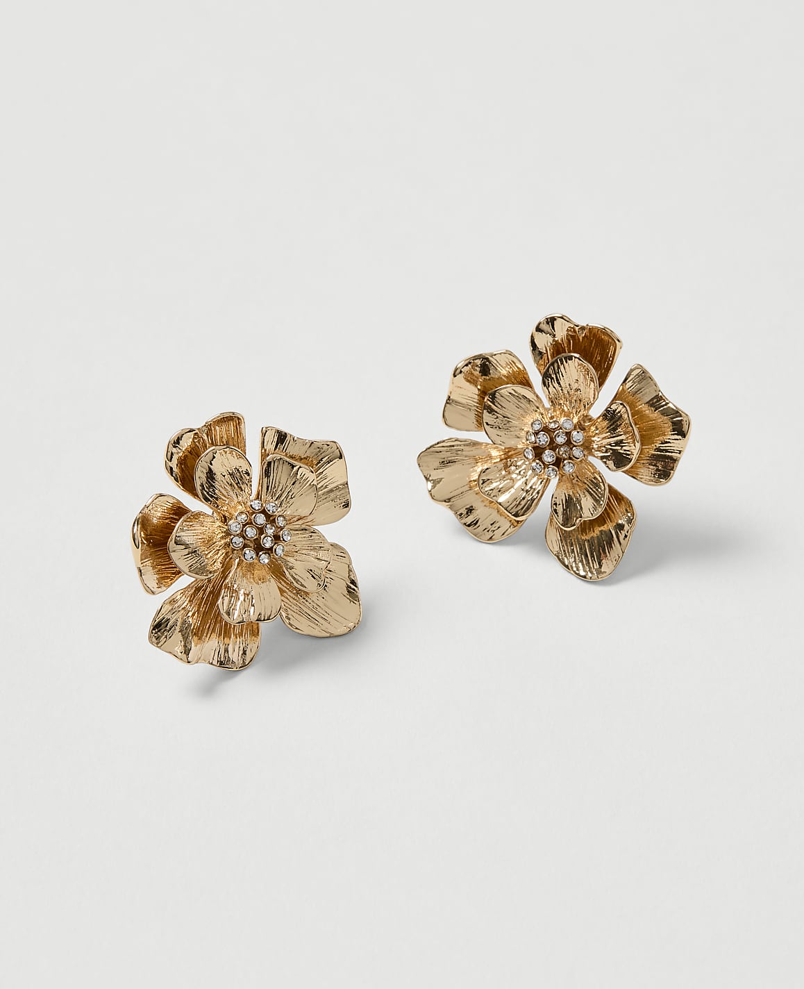 Two golden floral earrings with pearl centers rest on a plain white background.