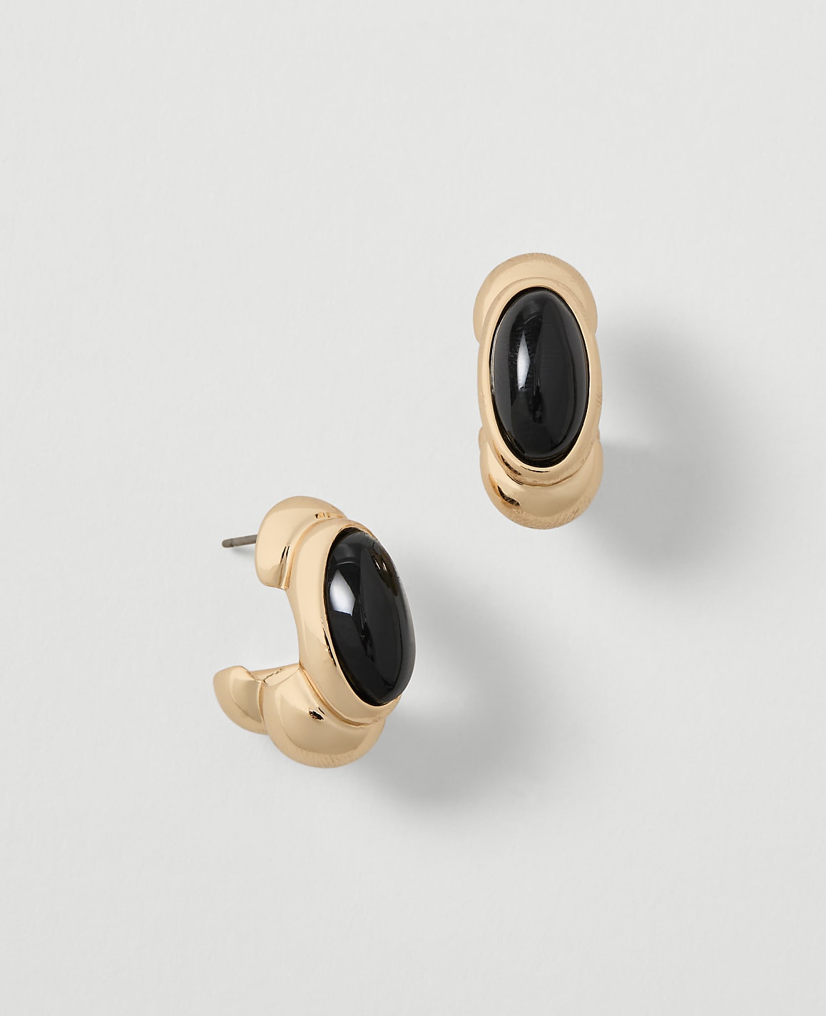A pair of gold hoop earrings with black oval stones are displayed against a plain, light gray background.