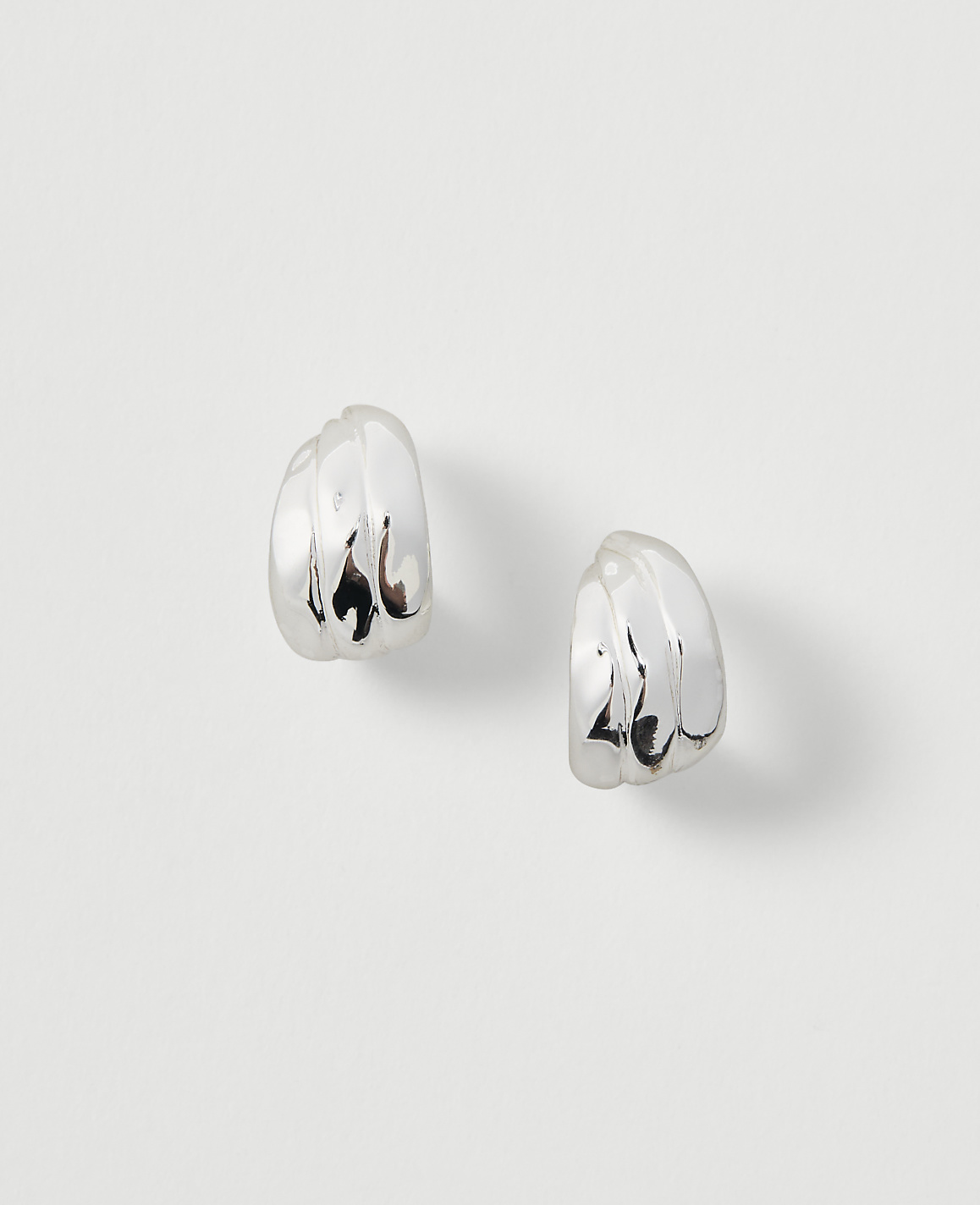 Two silver, ribbed hoop earrings rest on a plain, light gray background.