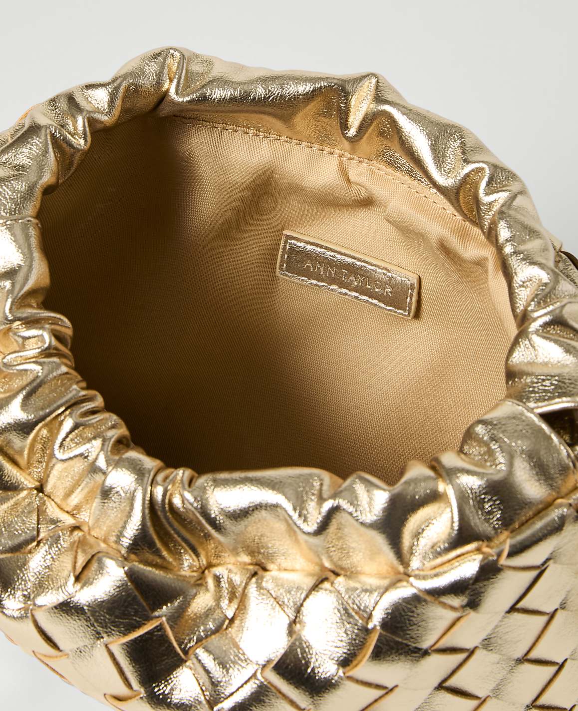 A metallic gold woven clutch with a cinched opening is presented against a plain white background.