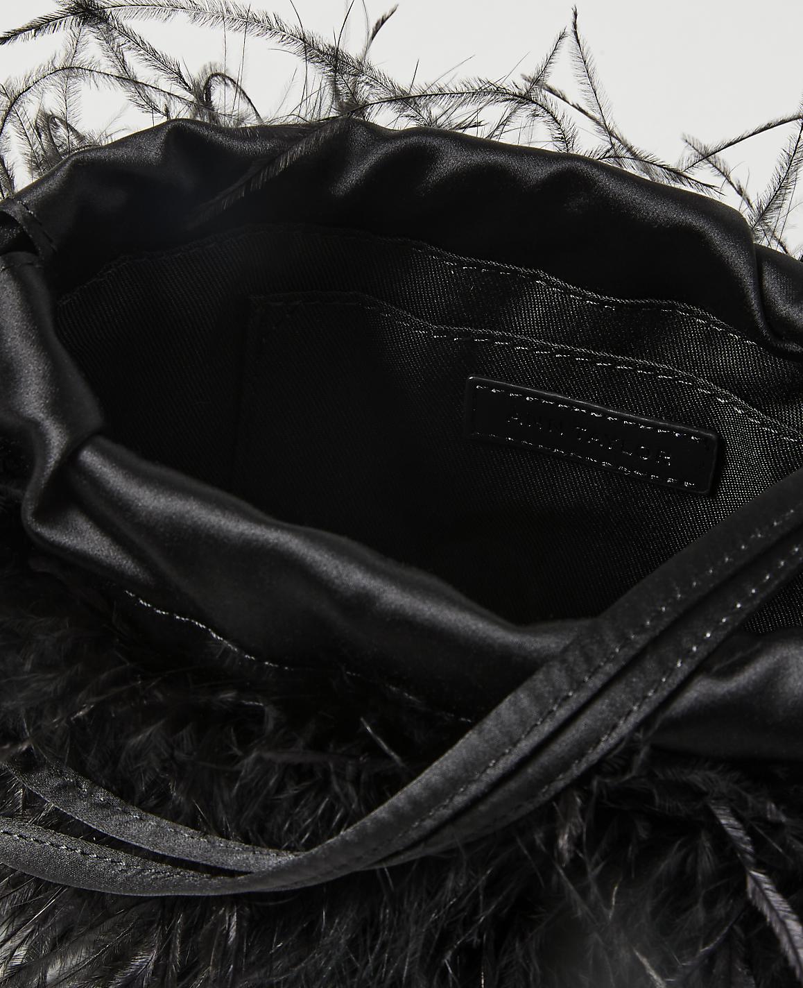 A black satin drawstring pouch bag adorned with black feathers in the foreground is set against a plain white background.