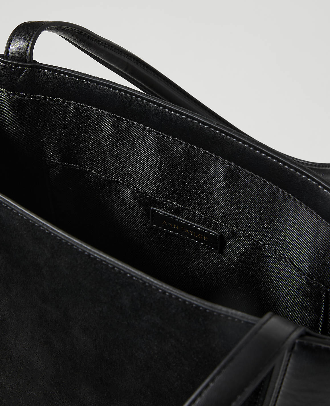 A black leather tote bag with a branded label is shown against a plain white background.