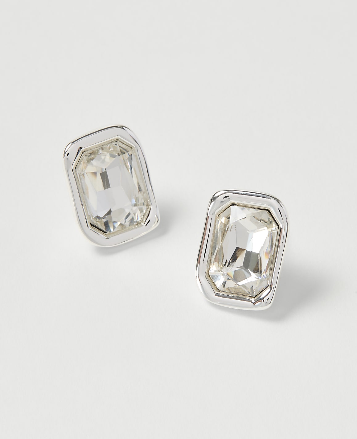 Two rectangular, clear gemstone earrings with silver settings rest on a plain white background.