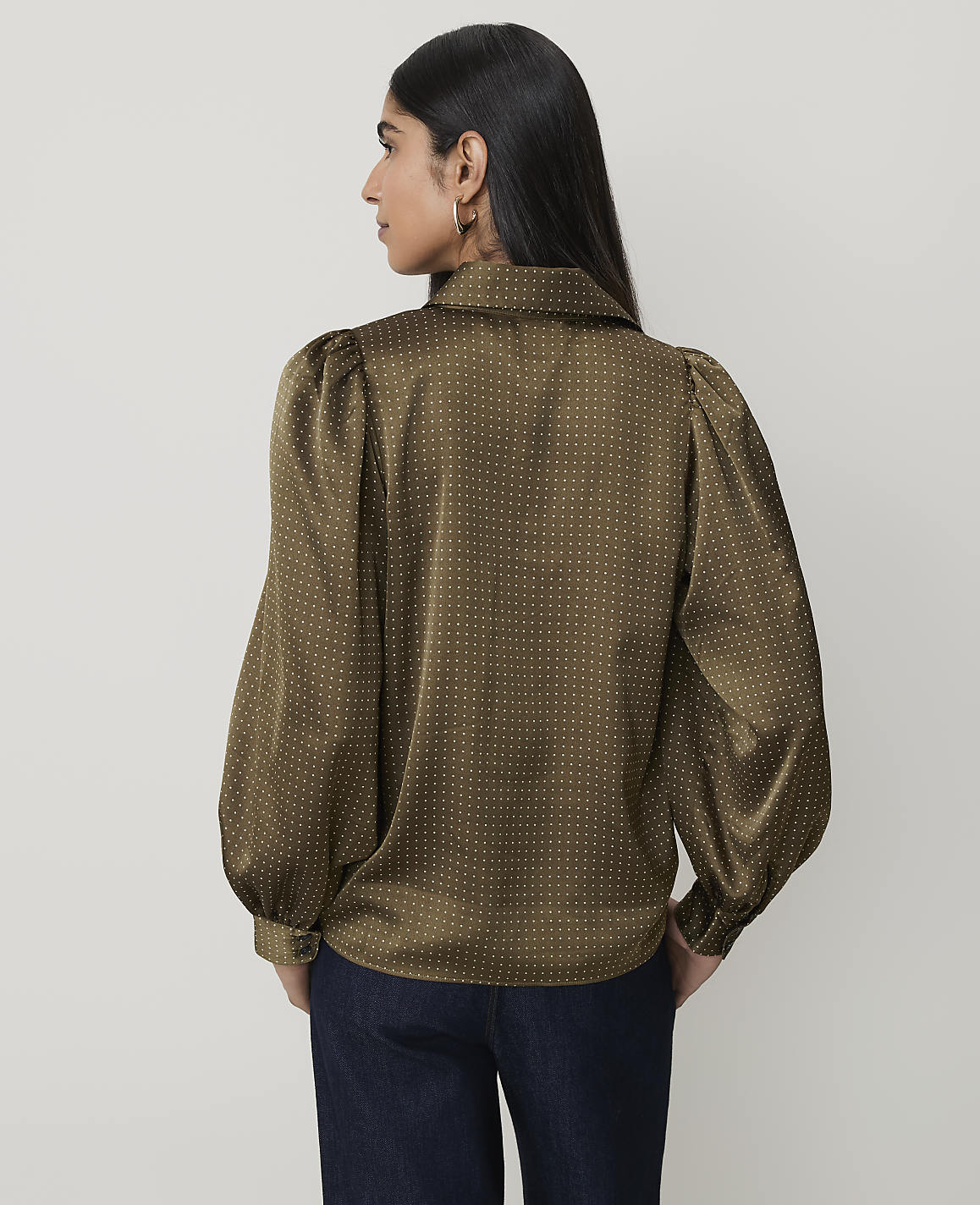 A woman in a polka-dot blouse stands against a plain background.
