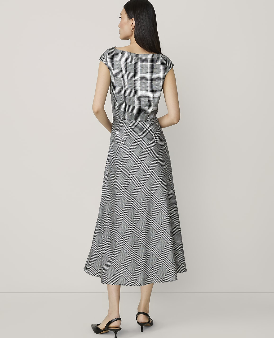 A woman in a plaid dress stands against a plain, light-colored background.
