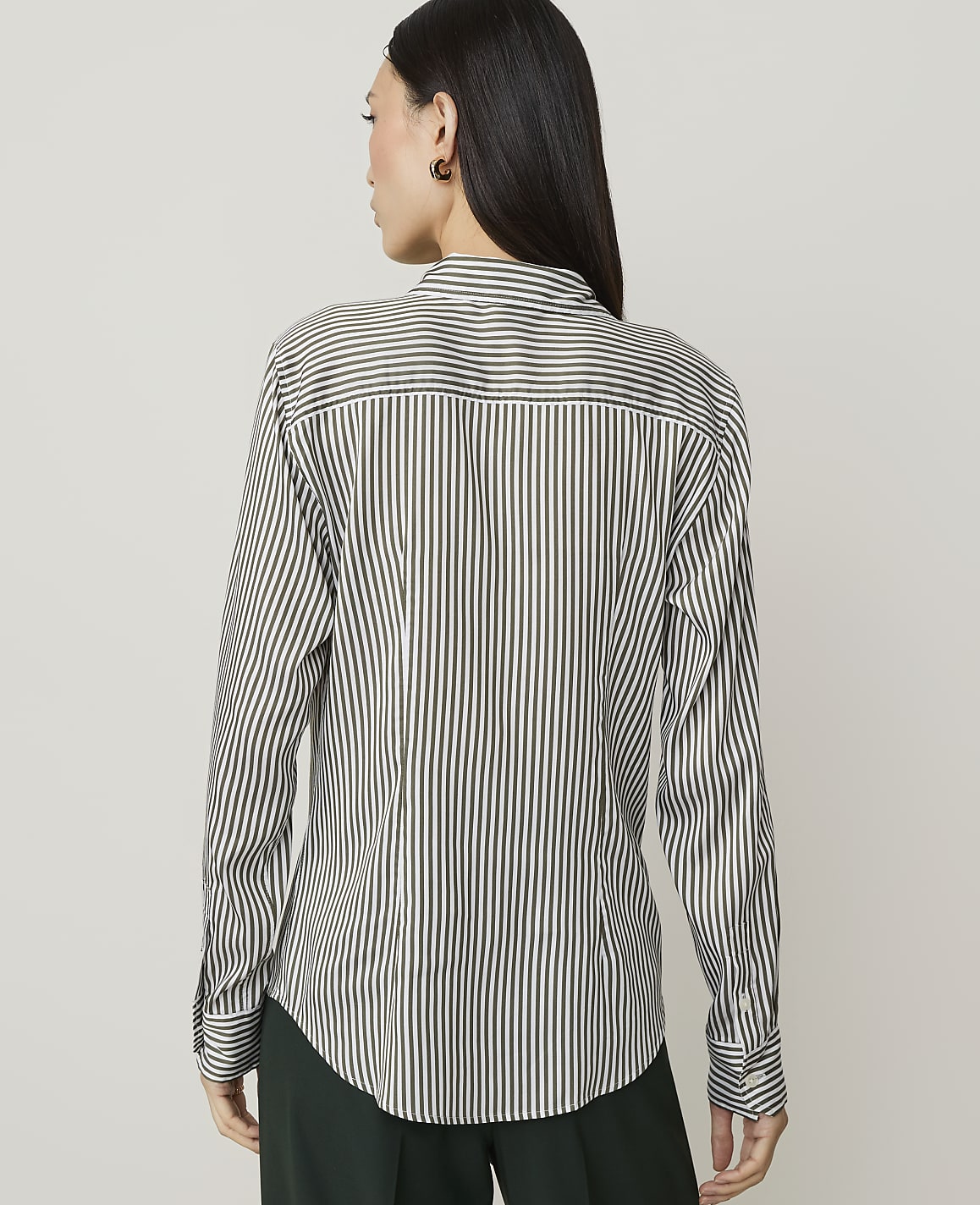 A woman in a striped shirt and brown skirt stands against a plain white background.