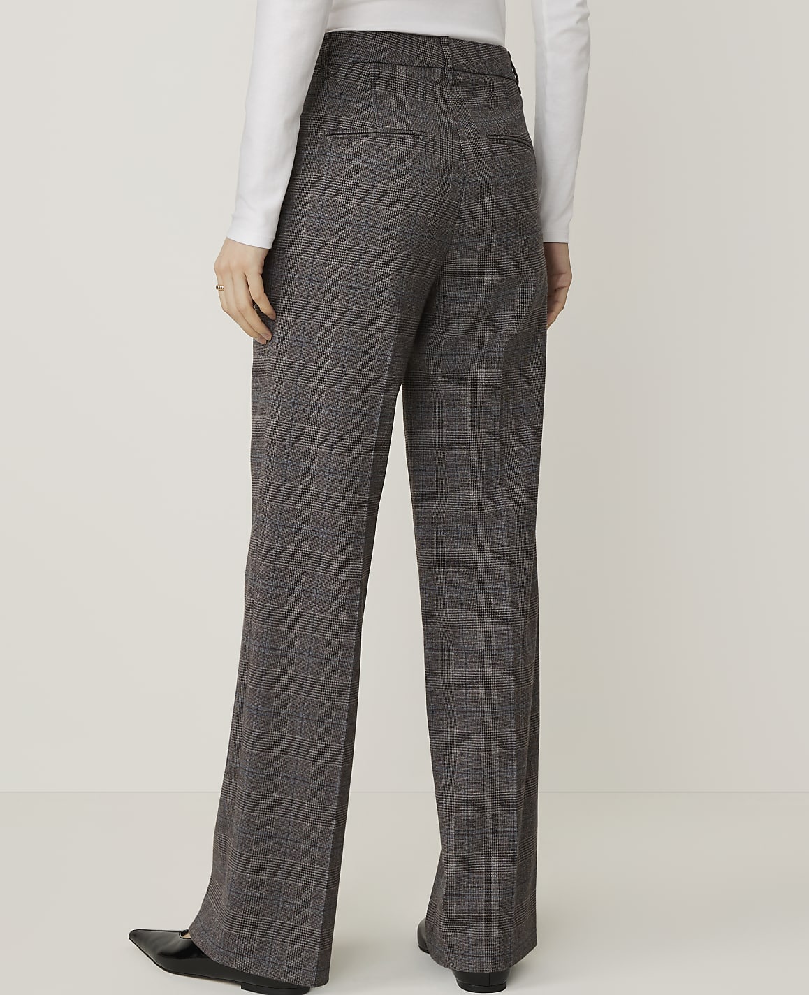 A person wearing plaid trousers stands against a plain white background.