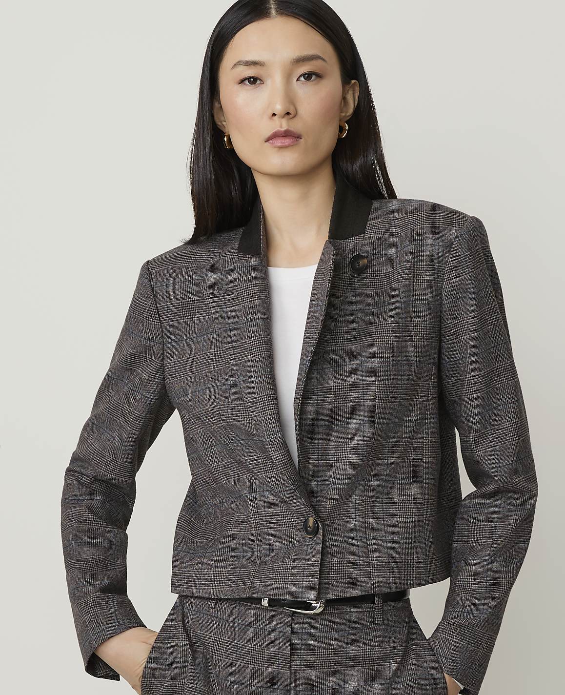 A woman in a plaid jacket and pants stands against a plain, light gray background.