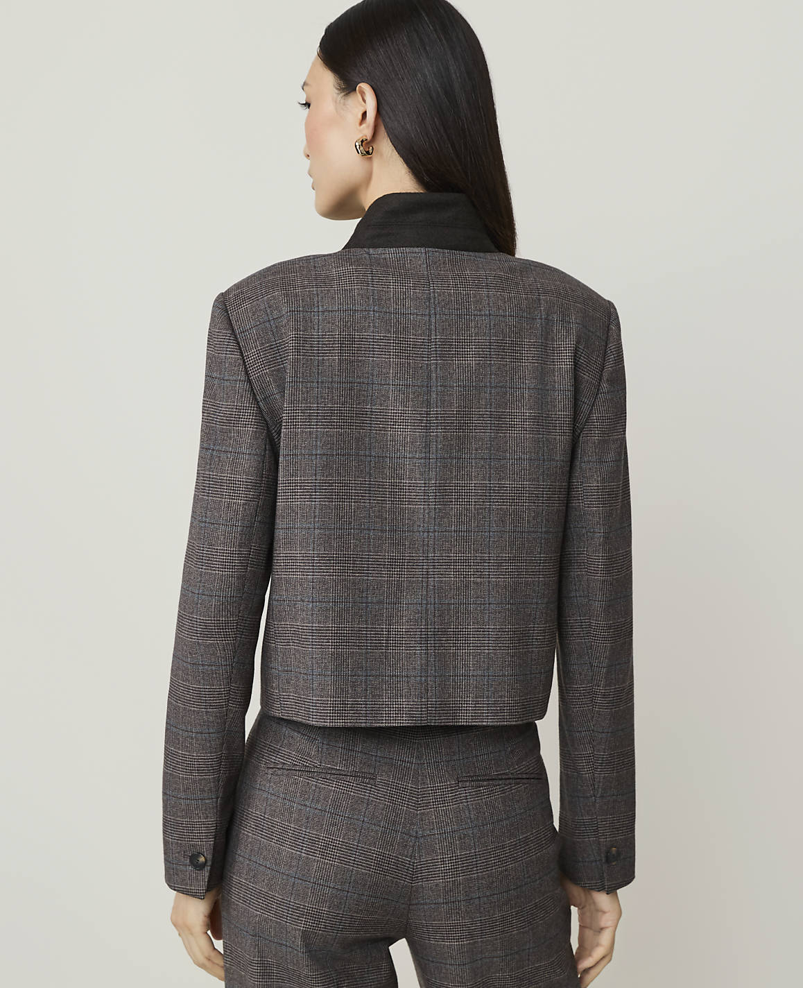 A woman in a plaid suit stands against a plain, light-colored background.