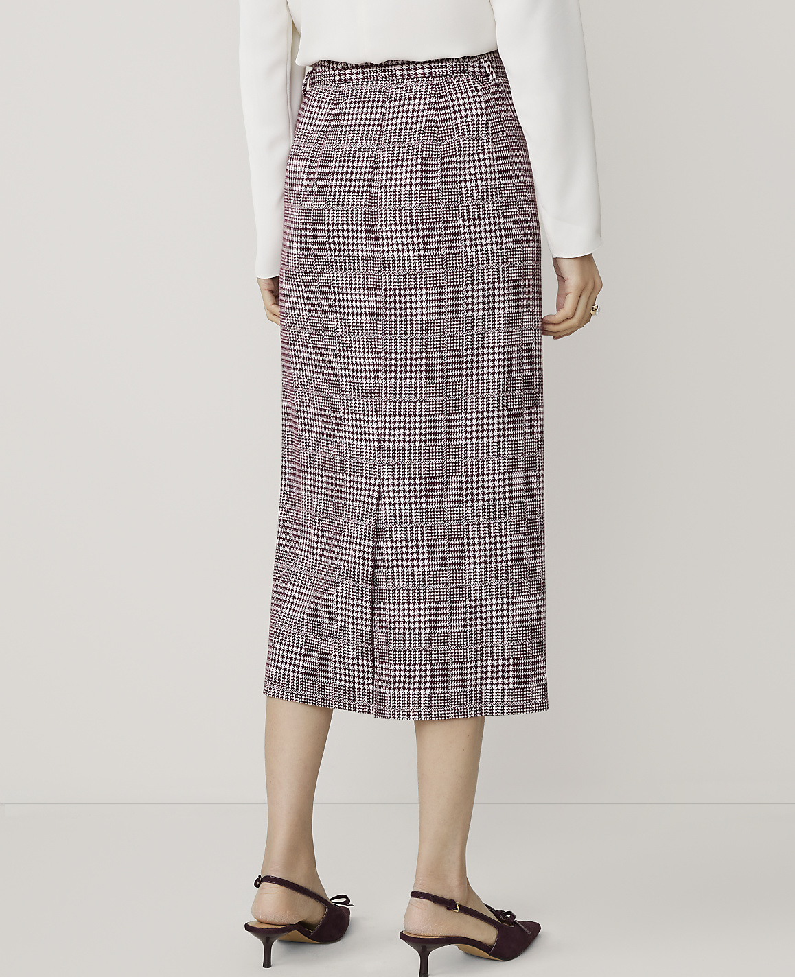 A person wearing a plaid skirt and heels stands against a plain white background.