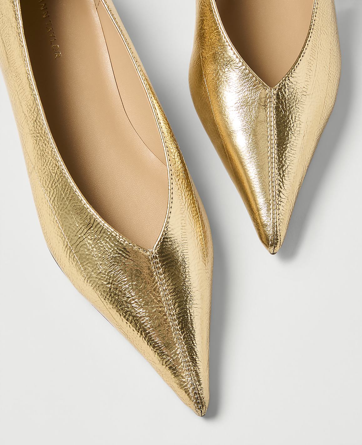 Two pointed, metallic gold flats with textured uppers are displayed against a plain white background.