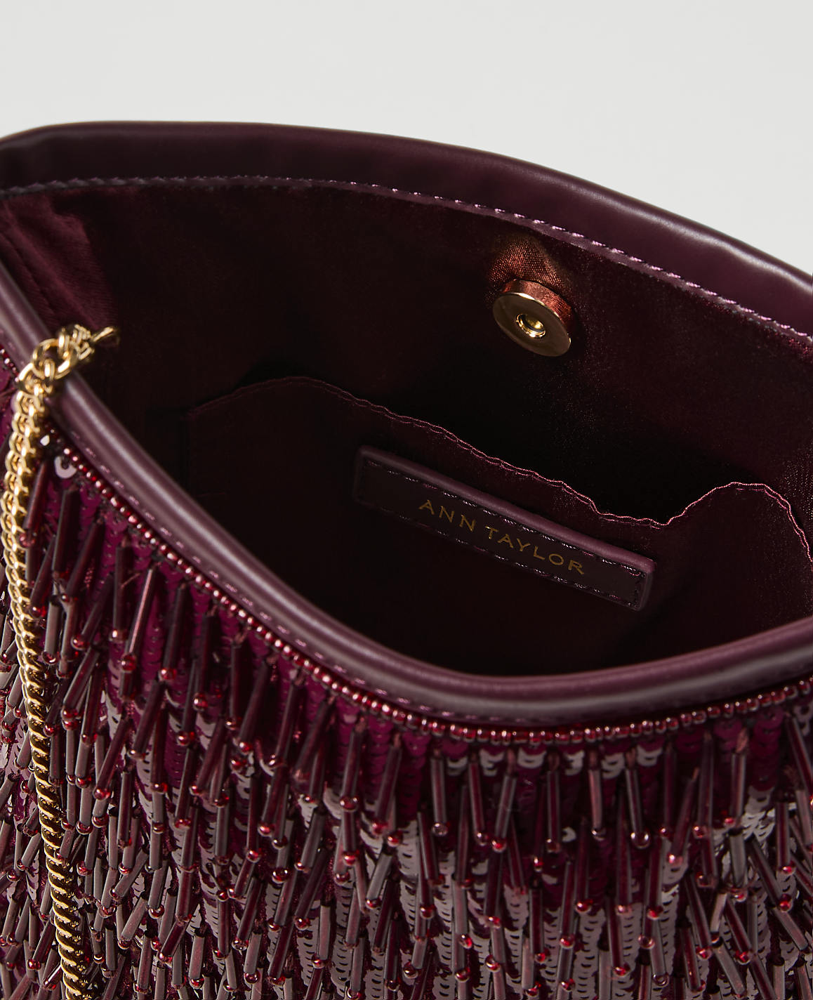 A deep red beaded clutch with a gold chain strap is open to reveal its interior, which has a small pocket with an Ann Taylor label.