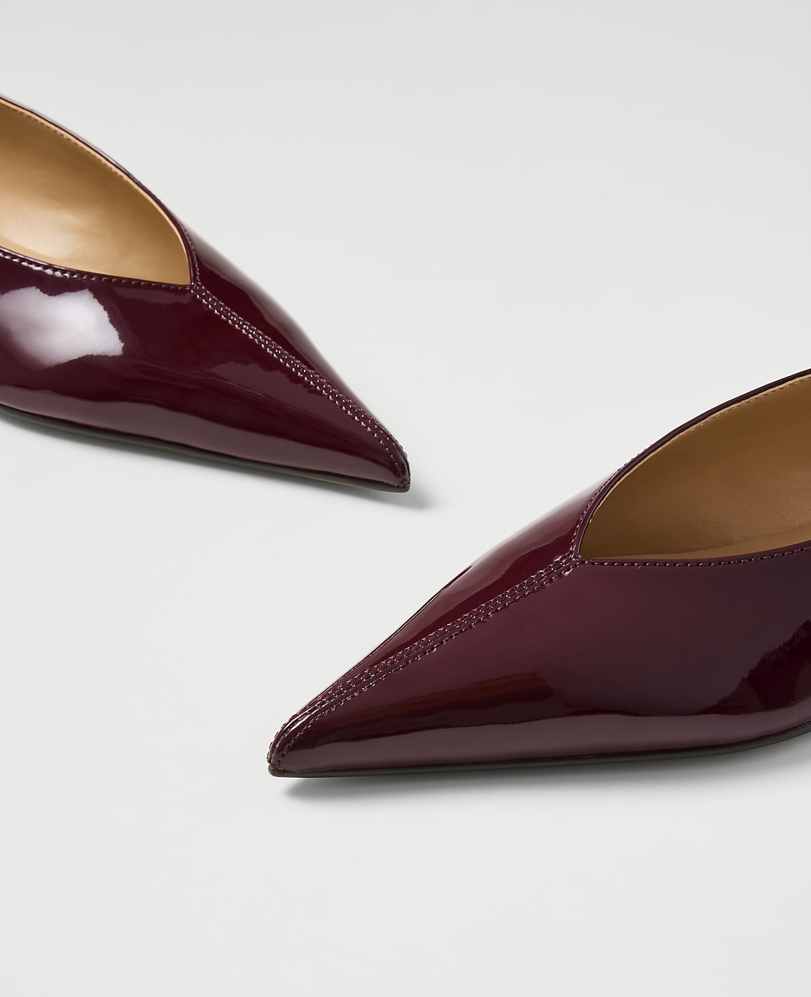 Two glossy burgundy pointed-toe flats rest on a plain white background.